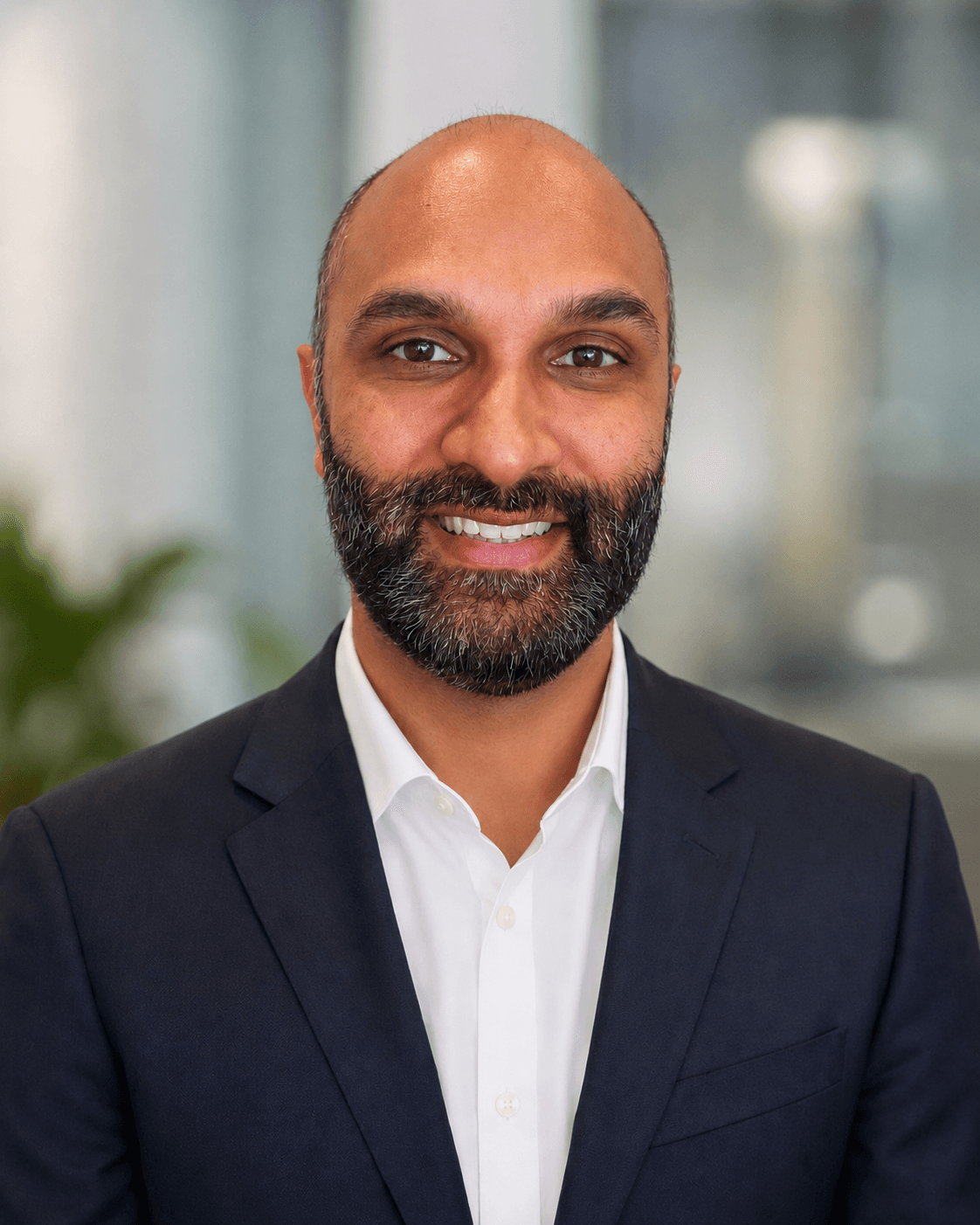 Smiling bald man with a dark beard wearing a navy blazer and white shirt.