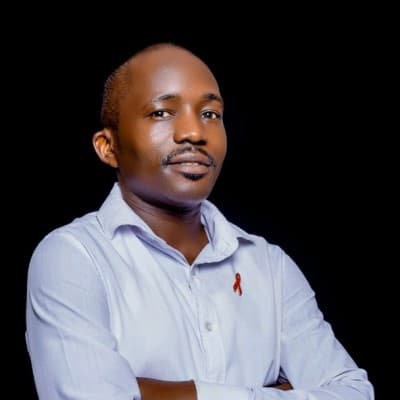 Black man with a mustache wearing a white shirt and red awareness ribbon against black.